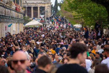 Kalabalık bir kalabalık bir meydanı, arka planda büyük sütunları olan bir binayla dolduruyor..