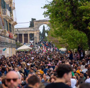 Tarihi mimari tarafından çerçevelenmiş bir kemer yoluna doğru ilerleyen büyük bir insan kalabalığı sokağı dolduruyor. Ağaçlar doğal bir element ekler..