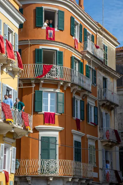 Dekoratif balkonları ve yeşil panjurları olan Avrupa binaları kırmızı kumaşla örtülmüş ve parlak gökyüzünün altında şenlikli bir atmosfer oluşturulmuştur..