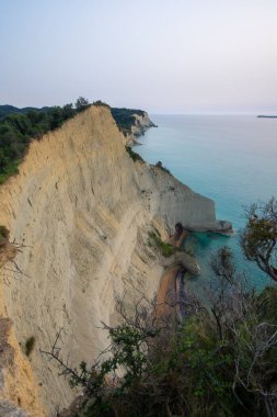Yüksek açı, yüksek bej kayalıkların, yeşil yaprakların ve dingin bir gökyüzünün altında canlı turkuaz okyanusun çarpıcı kontrastını yakalar..
