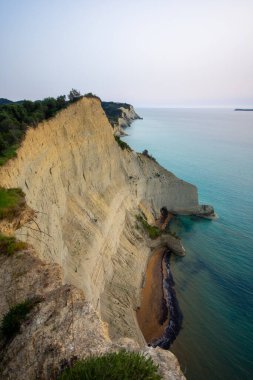 Denizin turkuaz sularına tepeden bakan yüksek kıyı uçurumlarının manzarası, en tepede yemyeşil yeşillik var. Alacakaranlıkta çekim yapılacak..