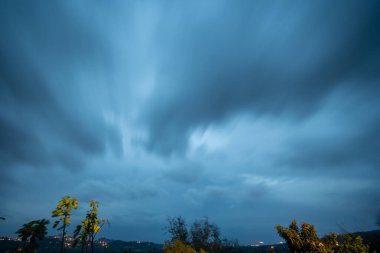 Çalkantılı bir gökyüzünün büyüleyici uzun pozlama sahnesi dramatik bulutlarla dolu, alacakaranlıkta loş bir manzaranın üzerinde..