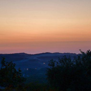 Uzaktaki yuvarlanan tepeler, sakin bir akşam gökyüzünün altında alacakaranlık gibi yumuşak pastel gölgelerle yakalanır..