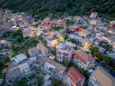 Ağaçlarla karışmış renkli binaları olan bir köyün hava görüntüsü. Alacakaranlığın yumuşak ışığı büyüleyici manzarayı güçlendirir..