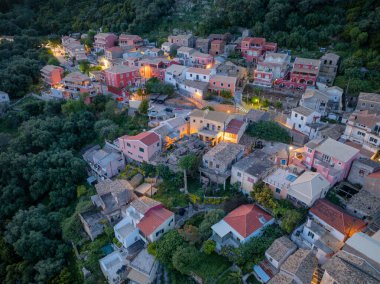 Alacakaranlıkta güzel bir Avrupa köyünü görüntüleyen bir anten, canlı binalar sergiliyor. Yeşillik içinde parıldayan ışıklar manzarayı aydınlatıyor..