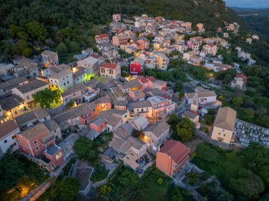 Yükseltilmiş bir perspektif yeşil yapraklarla çevrili tuhaf bir köyü yakalar. Binalar yumuşak akşam ışığında parlıyor, davetkar bir sahne yaratıyor..