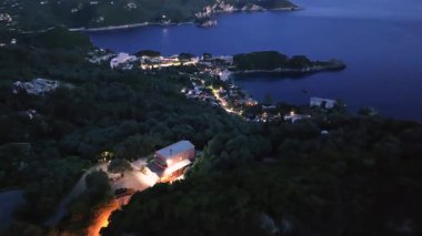 Geceleri kıyı kasabasının havadan görünüşü, karanlık ağaçların arasında parlayan ışıklar, denizle buluşan ışıklar. Paleokastritsa Korfu Adası, Yunanistan