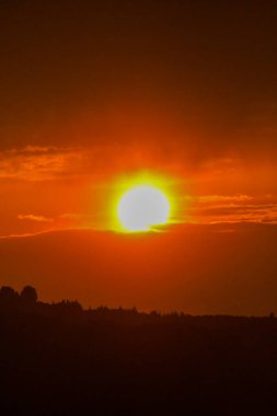 Güneşin atmosferde parlak turuncu bir şekilde parladığı büyüleyici bir gün doğumu. Kara silueti ve ufukta görünen ağaçlar..