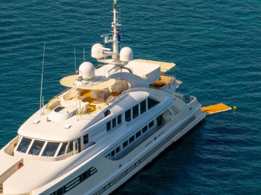 Lüks, büyük, beyaz bir yat, sakin, derin mavi sularda zarif bir şekilde yüzüyor. Mimari ayrıntıları modern deniz lüksüne işaret ediyor.