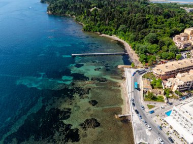 Havadan bakıldığında sakin bir körfezin yanında kıyı yolu, berrak sulara doğru uzanan uzun bir iskele, doğa ve kentselliği birleştiren.