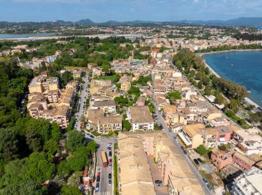 Yüksek açılı bir çekimde çatıları, ağaçlık yolları, uzak mavi denizi ve dağları olan bir Avrupa kasabası manzaralar sergiliyor..