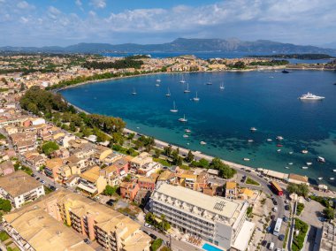 Deniz kenarında renkli evleri olan büyüleyici bir kıyı kasabası manzarası. Yelkenliler körfezi dolduruyor, uzak dağlar da arka planı sağlıyor..