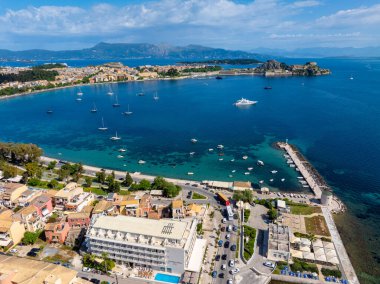 Manzarada canlı binaları olan bir kıyı kasabası berrak mavi sularda sayısız tekne ve uzak dağlardan oluşan bir zemin yer alıyor..