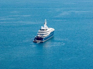 Büyük bir yat, berrak mavi okyanusa demirlemiş durumda. Yatın varlığı lüks, keşif ve denizcilik yaşam tarzını çağrıştırıyor..