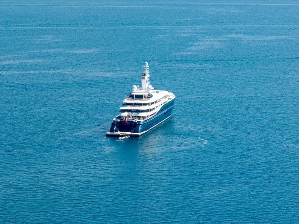 Büyük bir yat, berrak mavi okyanusa demirlemiş durumda. Yatın varlığı lüks, keşif ve denizcilik yaşam tarzını çağrıştırıyor..