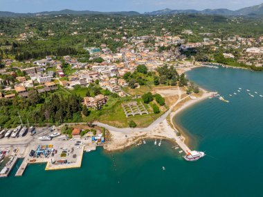 Yeşil tepelerle çevrili temiz turkuaz denizle karşılaşan bir kasabanın havadan görüntüsü. Tekneler kıyıya yanaştı. Binalar ve sokaklar görünür.