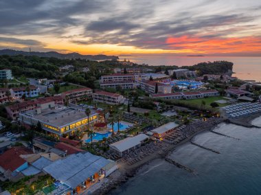 Bu manzaralı hava görüntülerinde, göletler, sahil, binalar ve huzurlu bir zemin sağlayan canlı bir günbatımı gökyüzü ile, alacakaranlıkta bir sahil tatil beldesi sergileniyor..