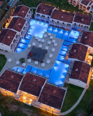 Havadan çekilen görüntüler, ışık saçan havuzları, oturma alanları ve şık yapıları olan bir tesis kompleksini ortaya çıkarıyor. Hepsi lüks bir gece manzarası yaratıyor..