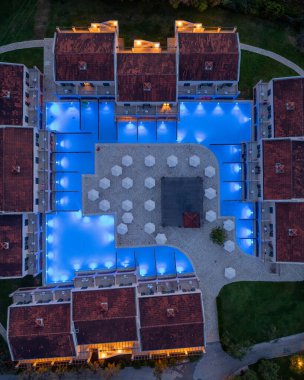 Gece çekimleri, havuzların, binaların, şemsiyelerin ve yol aydınlatmalarının yer aldığı sakin ve resimli bir ortam oluşturan bir tatil köyü olduğunu gösteriyor..