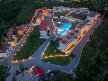 Yukarıdan yakalanan, alacakaranlık gösterilerinde aydınlatılmış bir tatil köyü. Renkli binalar, merkez havuz alanı ve yemyeşil yeşillikler..