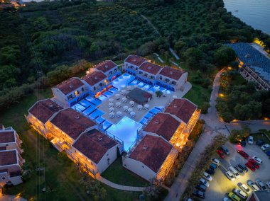 Lüks bir tatil köyünün çarpıcı hava manzarası. Tatil köyü yemyeşil, aydınlık havuzlar ve birden fazla park etmiş arabalarla çevrili..