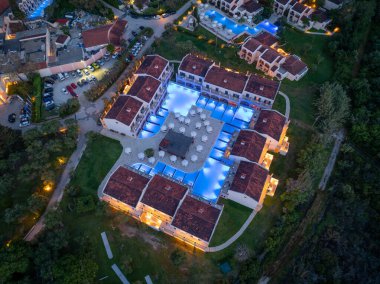 Hava çekimleri, birbirine bağlı havuzlar, kiremitli çatı villaları ve verimli, aydınlık peyzajlarla dolu, alacakaranlıkta lüks bir tatil beldesi sergiliyor..