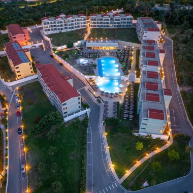 Hava perspektifi, aydınlık binaları ve verimli bir havuzu olan, verimli manzaralar ve yollarla çevrili bir tatil köyünü gösteriyor. Ortam sakin..