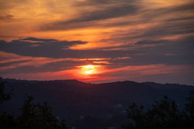 Büyüleyici bir günbatımı sahnesi. Sıcak renkler gökyüzünü aydınlatıyor. Dalgalanan tepeleri aydınlık ufka, doğanın sanatını yansıtıyor..