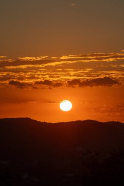 Canlı bir günbatımı manzarayı sıcak, turuncu ışıkla kaplar. Uzak tepeler parlak gökyüzüne karşı gölgelenmiş, huzur verici bir manzara yaratıyor..