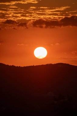 Canlı bir günbatımı gökyüzünde sıcak, altın bir parıltı bırakır, tepeleri siluete alır ve alacakaranlıkta sakin, resimsel bir manzara yaratır..