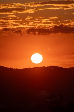 Görüntü, gün batımının canlı renklerini yakalar ve manzaranın üzerine sıcak bir parıltı saçar. Yuvarlanan tepelerin silueti gökyüzüne karşı.