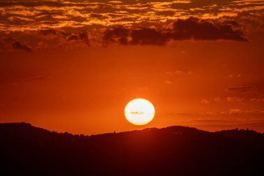 Güneş, siluetli tepelerin üstündeki çerçevenin merkezinde turuncu gölgeler ve huzur dolu bir an yaratıyor..