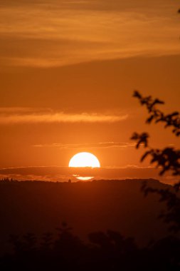 Işıl ışıl güneş ufkun altına batar, sıcak, turuncu bir parıltı yayar gökyüzünde, bir kara silueti gibi görünür.