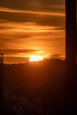 Güneş ufukta batmaya başladığında parlak ve canlı bir turuncu gökyüzüne karşı bir kara silueti resmedilir..