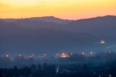 Manzaralı bir manzara alacakaranlıkta bir vadi gösteriyor. Hilly siluetleri uzakta. Işıklar aşağıdaki bir kasabayı aydınlatıyor. Sis vadiyi kaplıyor.