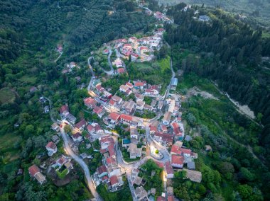 Havadan bakıldığında, kırmızı çatılı binalar, dolambaçlı yollar ve canlı yeşillikleri olan büyüleyici bir köy görülüyor. Sahne huzuru çağrıştırıyor.
