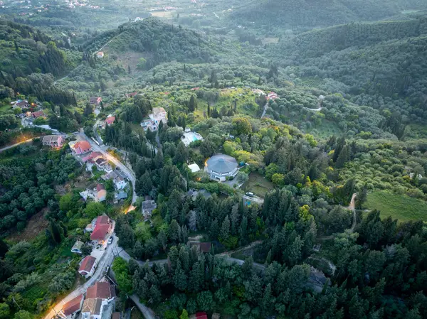 Yoğun, yeşil ağaçlarla kaplı bir yamaçta yuva yapmış ev ve yolların havadan görünüşü. Manzara doğal ve huzurlu, huzurlu bir ortam..
