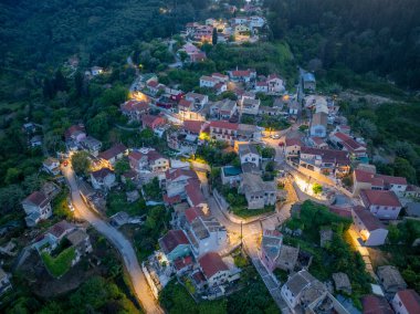 Kuş bakışı bakış açısı, yeşil bir yamaçta yuva yapmış, evleri ve yolları sıcak akşam ışıklarıyla aydınlanan tuhaf bir köy olduğunu gösteriyor..