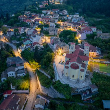 Alacakaranlıktaki bir tepedeki köyün manzarası. Evler ve binalar manzarayı noktalarken, odak noktası bir kilise.. 