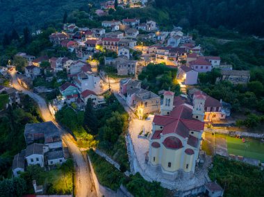 Huzurlu bir yamaç köyü, renkli çatıları olan geleneksel evleri sergiliyor, alacakaranlık karanlık gökyüzünün altında sokak lambalarıyla aydınlatılıyor..