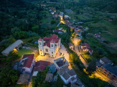 Sakin bir hava manzarası, alacakaranlıkta alacakaranlıkta belirgin bir şekilde aydınlatılmış, yuvarlanan tepelerin ve etrafındaki çatıların arasında duran bir kilisenin bulunduğu tuhaf bir köyü yakalıyor..
