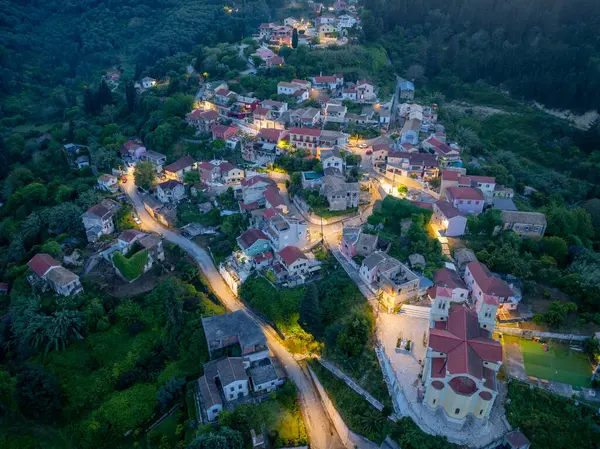 Bir hava görüntüsü, yeşil bir yamaçta kurulmuş büyüleyici bir köyü ortaya çıkarıyor. Alacakaranlık ve sokak ışıklarının sıcacık ışığıyla aydınlatılıyor..