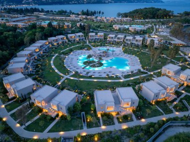 Tepe manzaralı lüks villalar. Palmiye ağaçları, şezlonglar ve okyanus manzaralı büyük bir havuz kompleksi. Hepsi alacakaranlıkta aydınlandı..