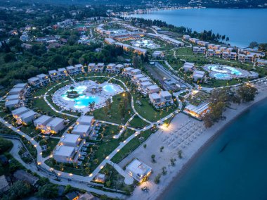 Hava perspektifi, alacakaranlıkta deniz kenarında lüks bir tatil köyü yakalar. Birden fazla havuz, konaklama ve plaj alanı gösterilir..