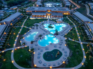 Büyük bir havuz kompleksi, açık hava alanları ve lüks mimari tasarımı ön plana çıkaran çarpıcı bir tatil köyünün gece manzarası. Işık güzelliği arttırır..