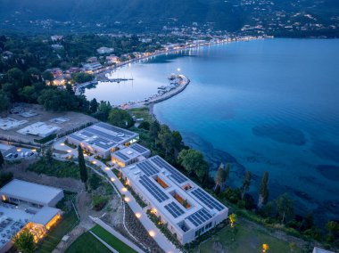 Sahil boyunca güneş panelleri olan modern binaları gösteren, büyüleyici bir kasabanın ve sakin bir limanın zeminine bakan bir hava görüntüsü..