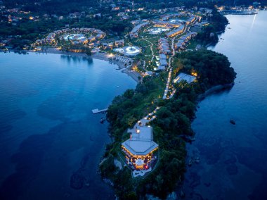 Alacakaranlıktaki lüks bir tatil köyünün nefes kesici hava manzarası, denizle çevrili bir yarımadada, sıcak ortam aydınlatmasıyla aydınlatılıyor..