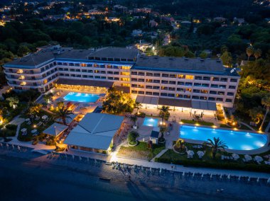 Aydınlatılmış bir tatil köyü, birden fazla havuz, bereketli peyzaj ve rahatlatıcı bir atmosfer için yumuşak ışıklandırma içeren kumsalla akşam karanlığında buluşur..