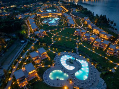 Gece gökyüzüne karşı aydınlanan varlıklı bir tatil köyünün havadan görünüşü. Bahçe düzenlemeleri havuzlar ve yumuşak ışıklandırmalarla kaplıdır..