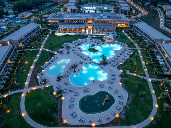 Büyük bir havuz kompleksi, açık hava alanları ve lüks mimari tasarımı ön plana çıkaran çarpıcı bir tatil köyünün gece manzarası. Işık güzelliği arttırır..